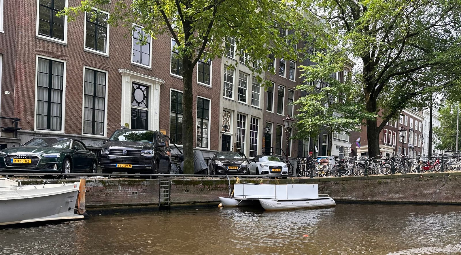 Amsterdam canal street with parked cars, bikes, and boats