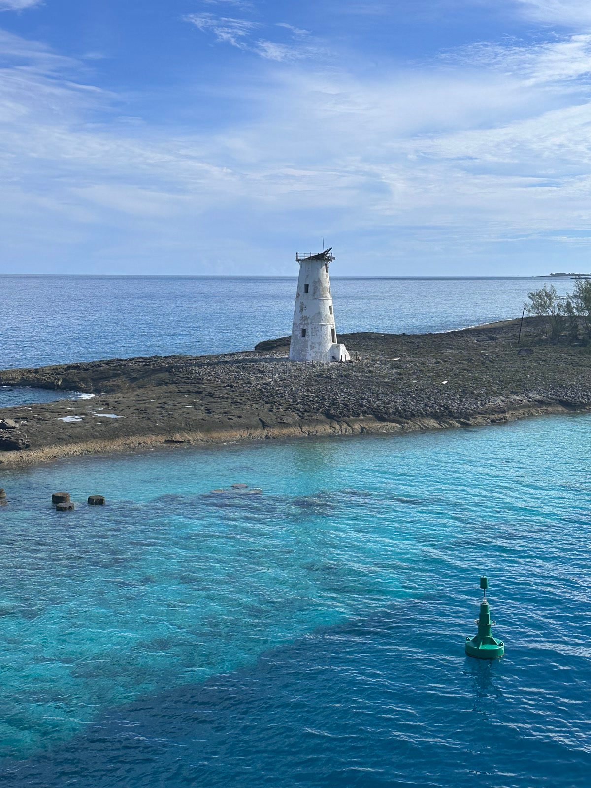 Weathered white Hog Island Lighthouse on a rocky spit in turquoise Nassau Harbor