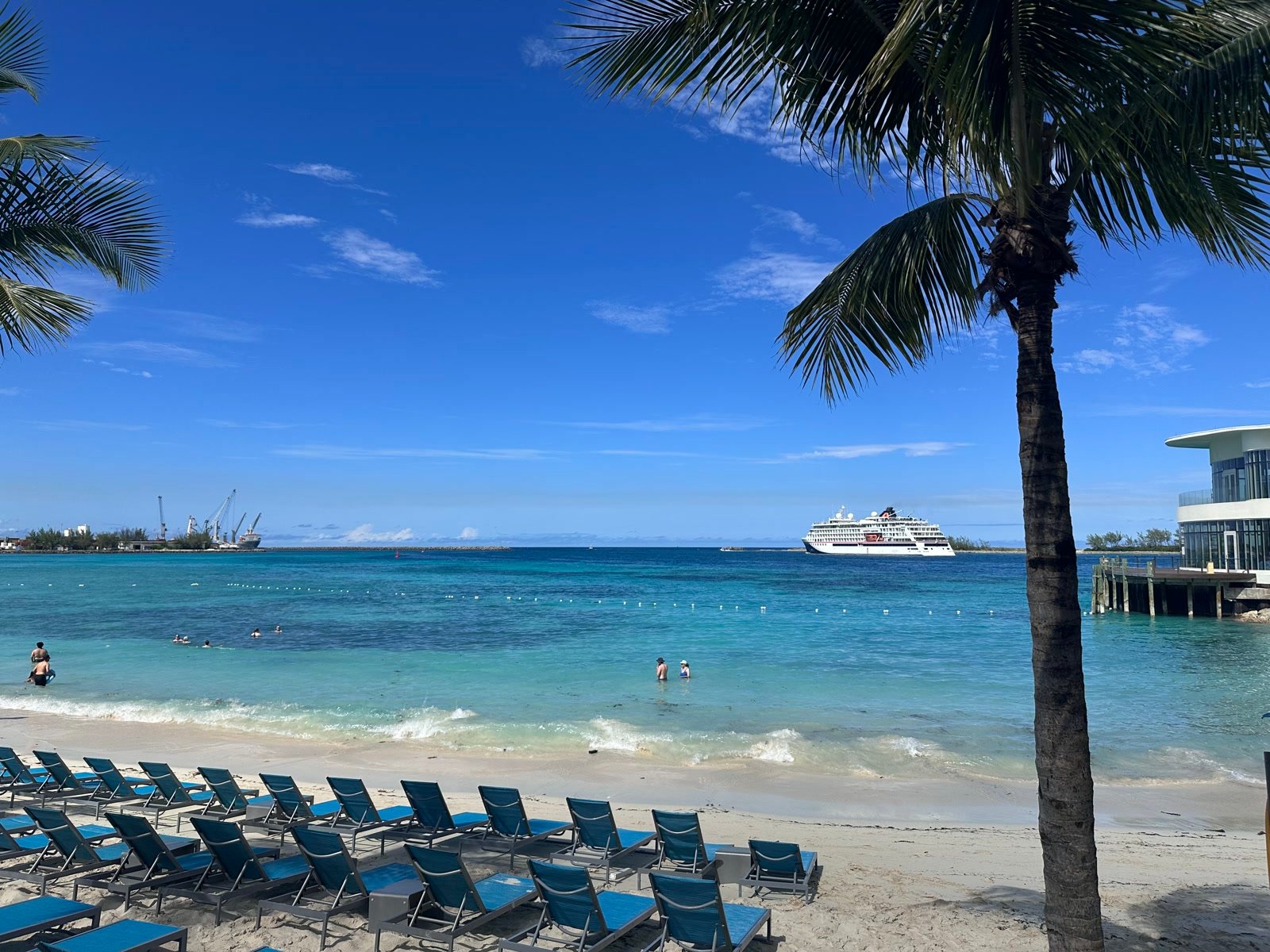 Turquoise Bahamian beach with lounge chairs, palms, and a cruise ship on the horizon
