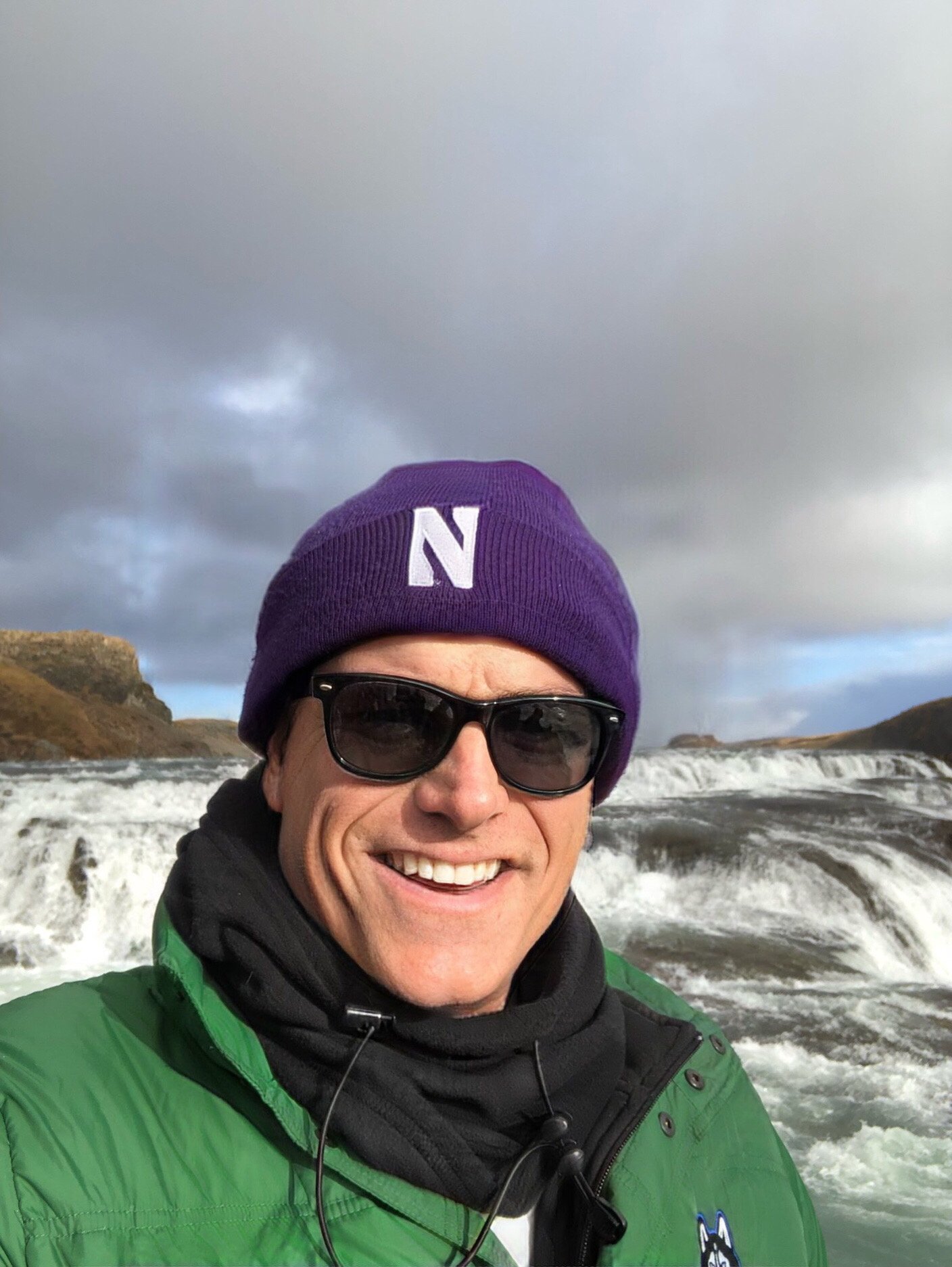 Chuck smiling in front of a powerful Icelandic waterfall
