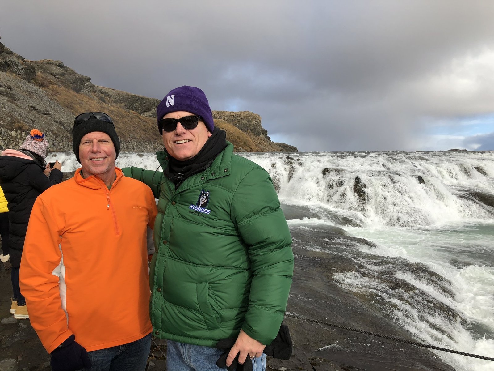 Chuck and a friend smiling in front of a wide waterfall