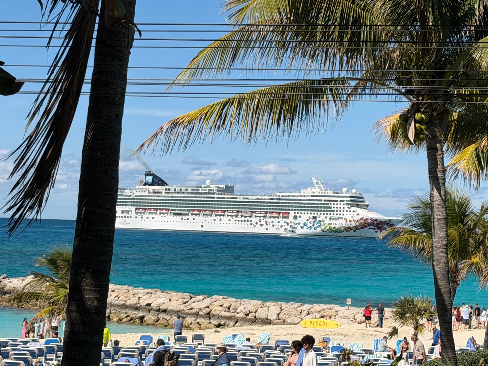 The Norwegian Gem offshore beyond beach lounge chairs and palms