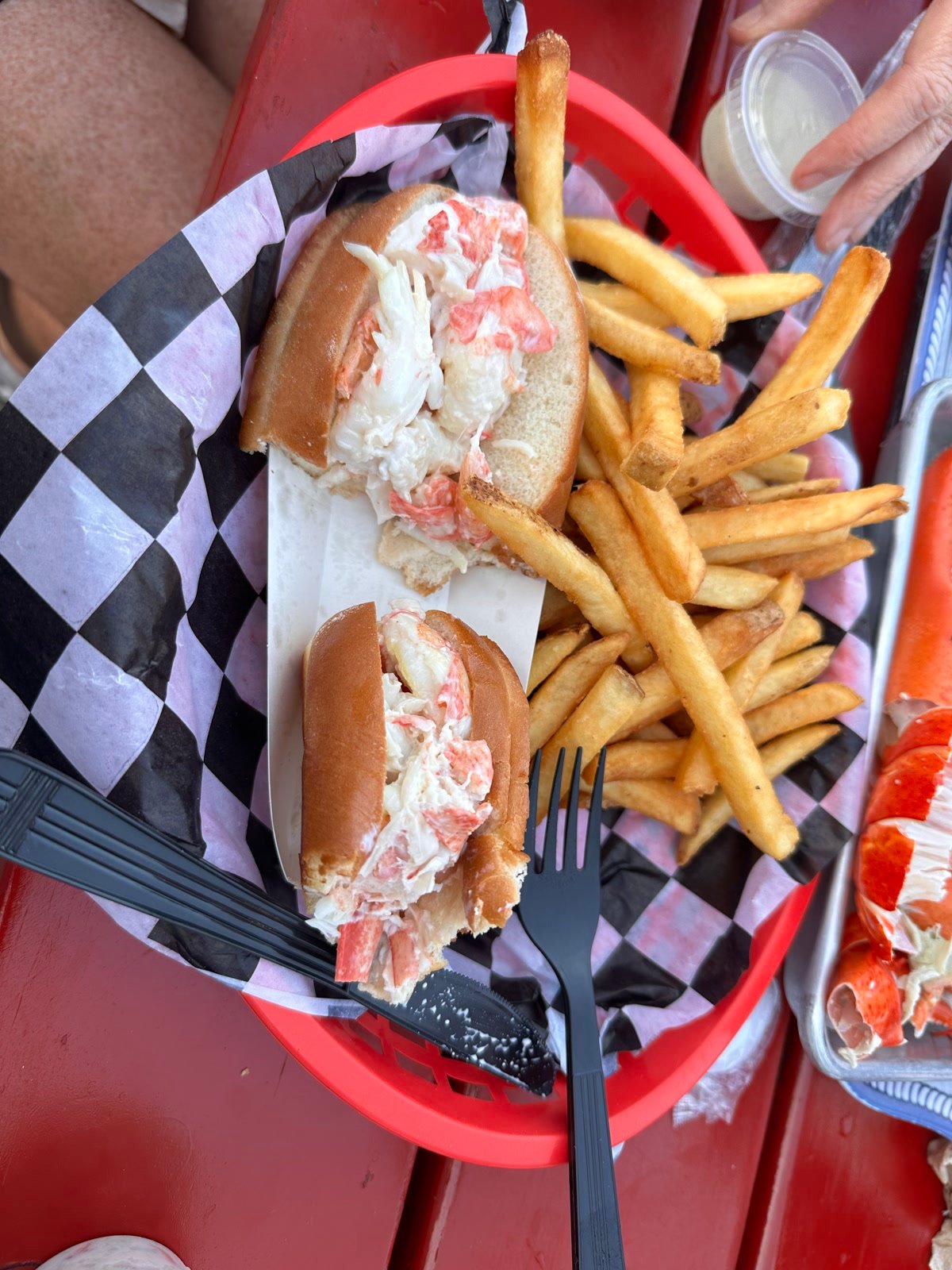 Lobster rolls and fries in a basket on a red picnic table