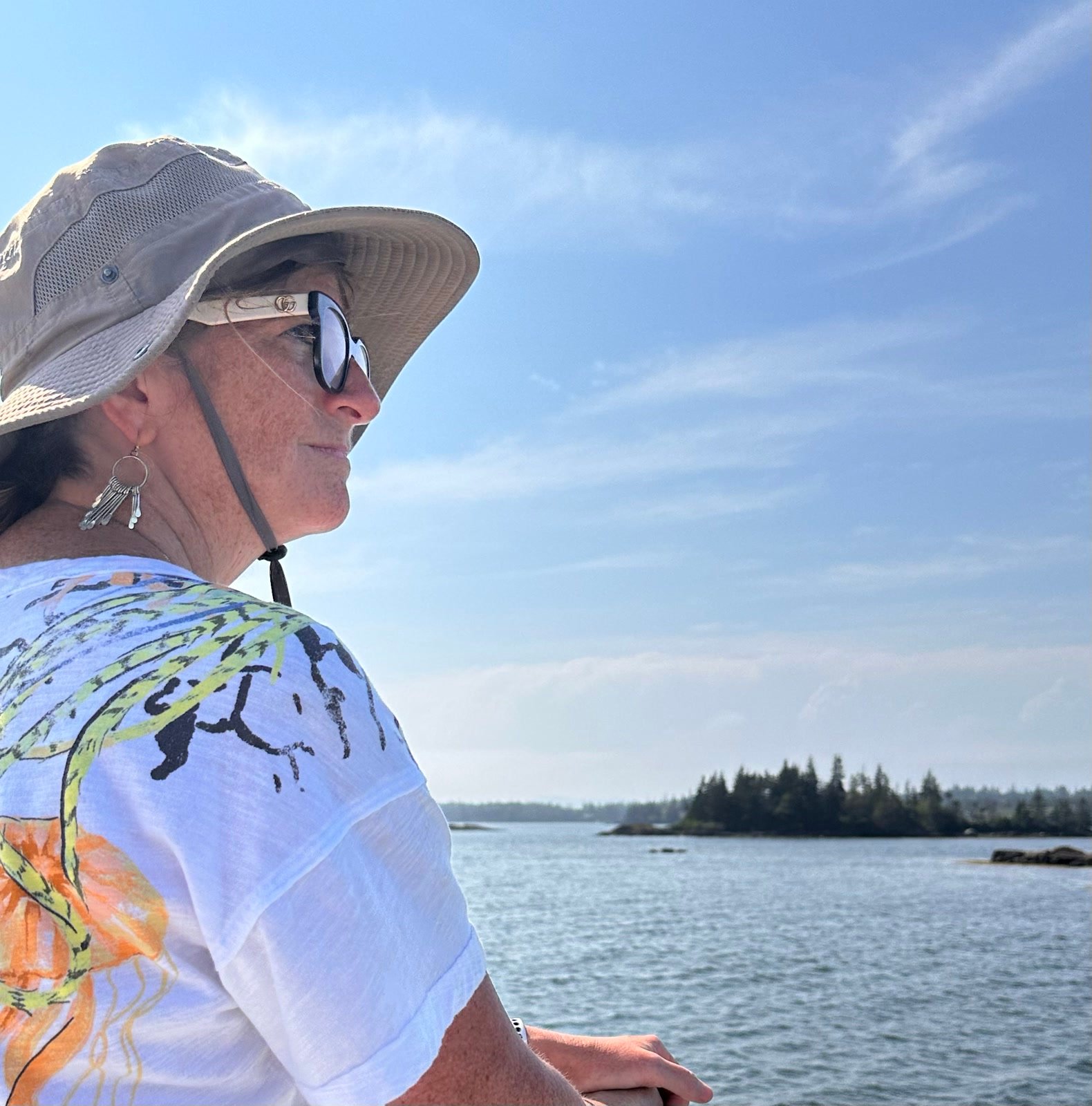 Traveler in a sun hat looking toward a pine-covered Maine island